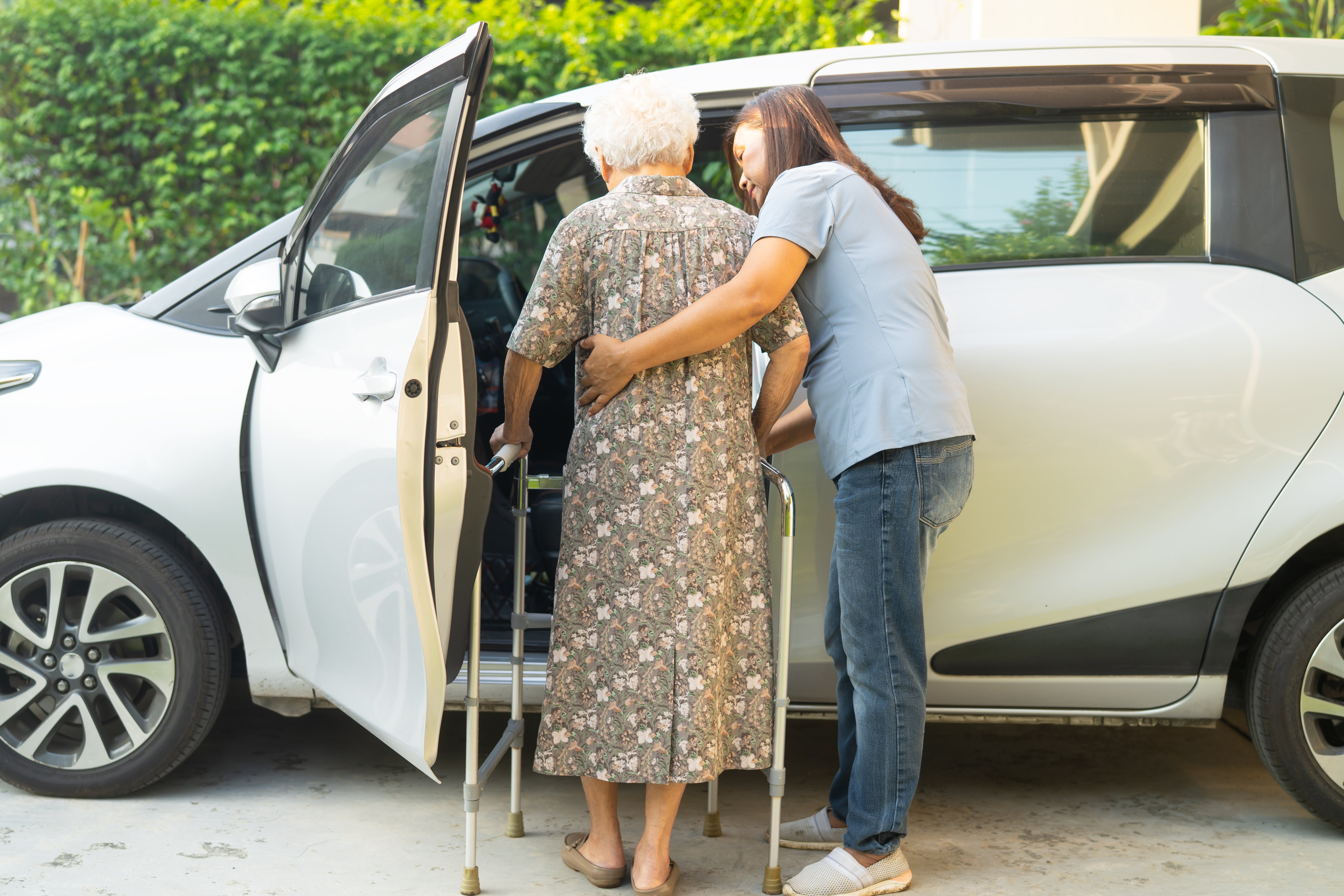 Caregiver help Asian elderly woman disability patient get into car.